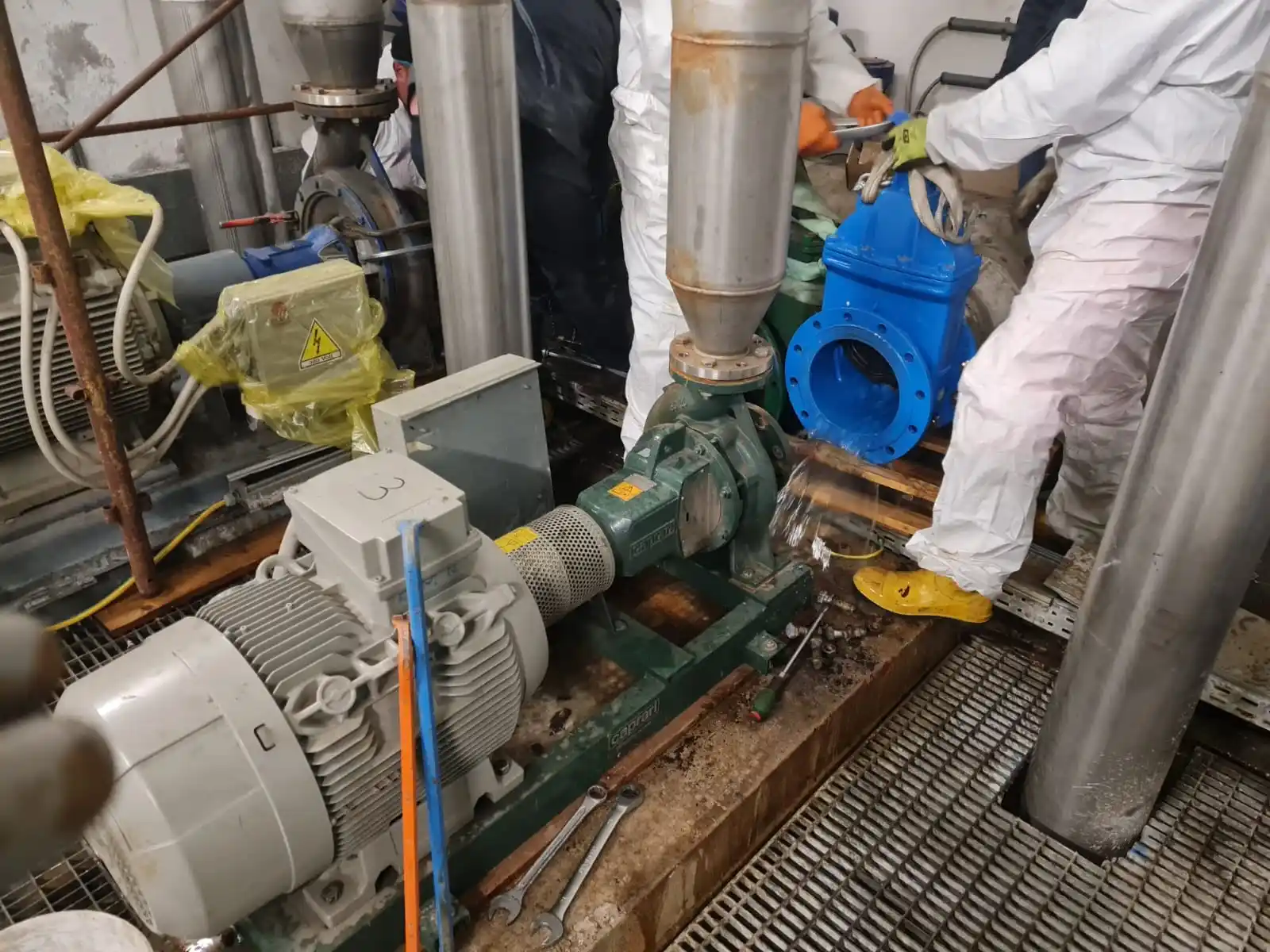 Questa è un'immagine di una pompa industriale con una valvola a farfalla in primo piano. La pompa è collegata a un motore elettrico e la valvola a farfalla è collegata a una tubatura. Si possono vedere alcuni lavoratori che si occupano della manutenzione della pompa e della valvola a farfalla.