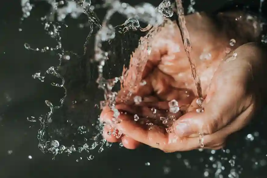 Una persona si lava le mani con acqua che schizza. L'acqua crea motivi unici mentre cade dalle mani.