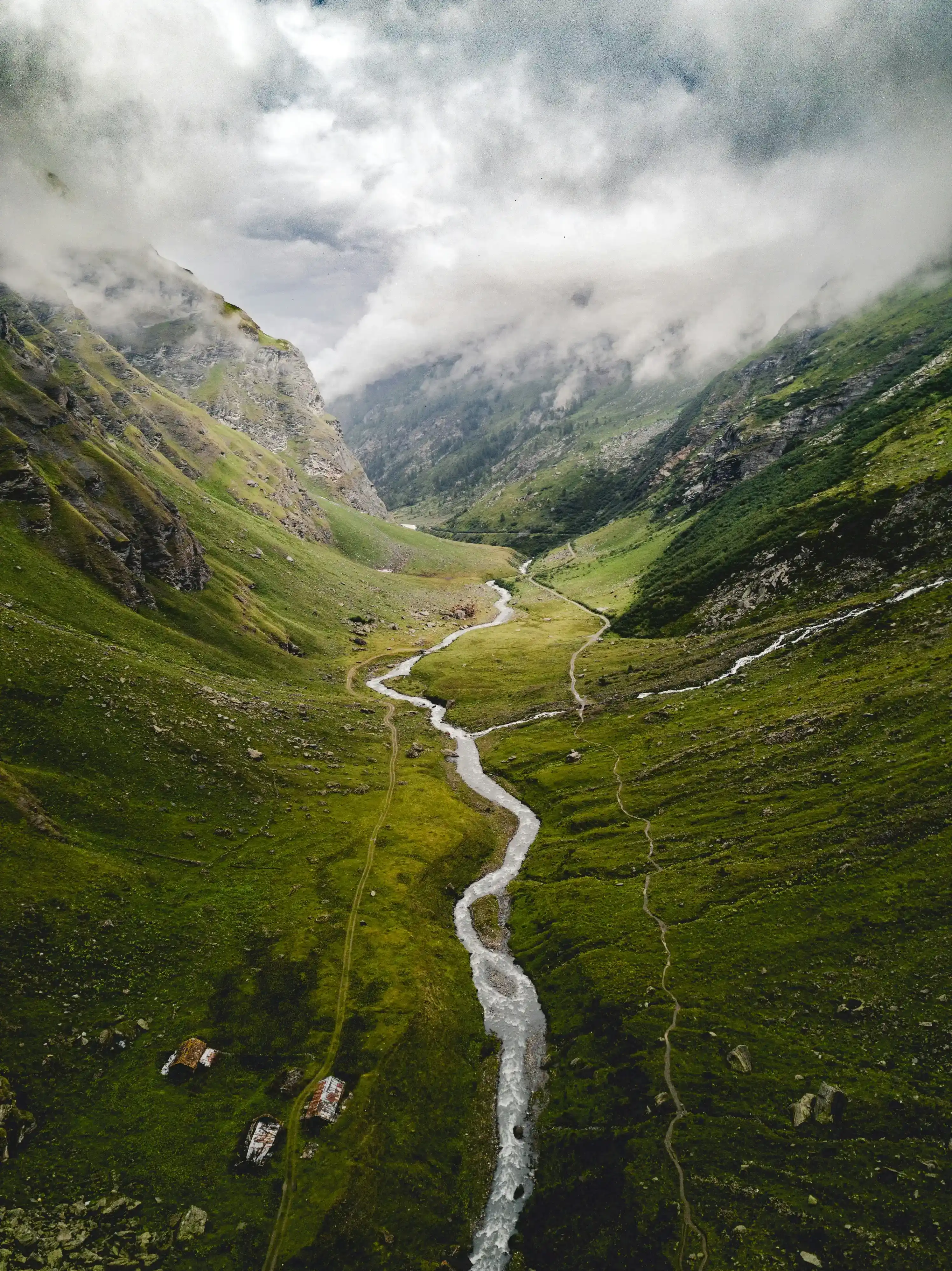 Una vista aerea di un fiume che scorre attraverso una valle montuosa. Il fiume è circondato da una vegetazione verde lussureggiante e le montagne sono ricoperte di nebbia.