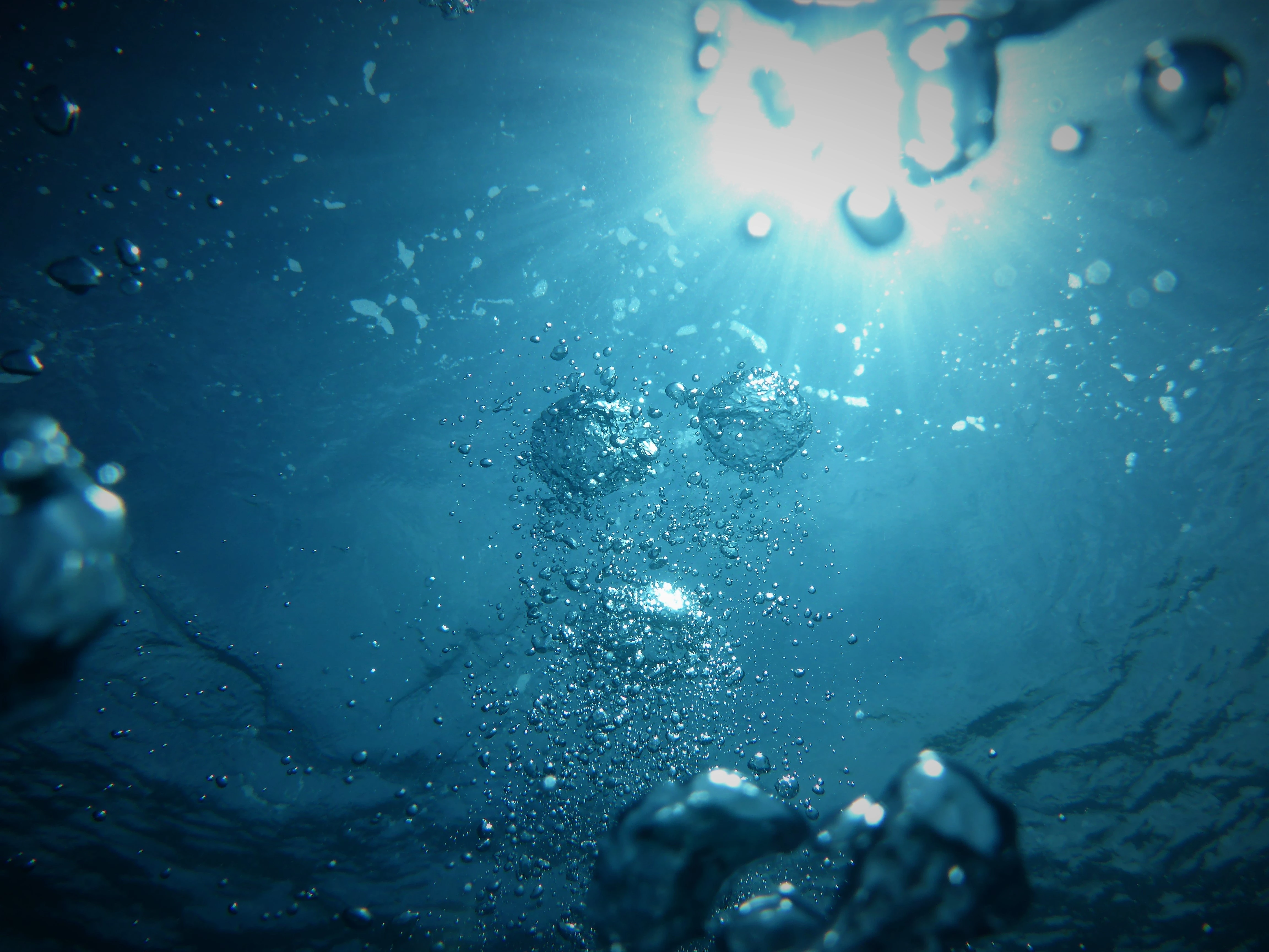 Un gruppo di bolle d'aria sale attraverso l'acqua blu. La luce del sole brilla attraverso le bolle dall'alto, creando un effetto scintillante.