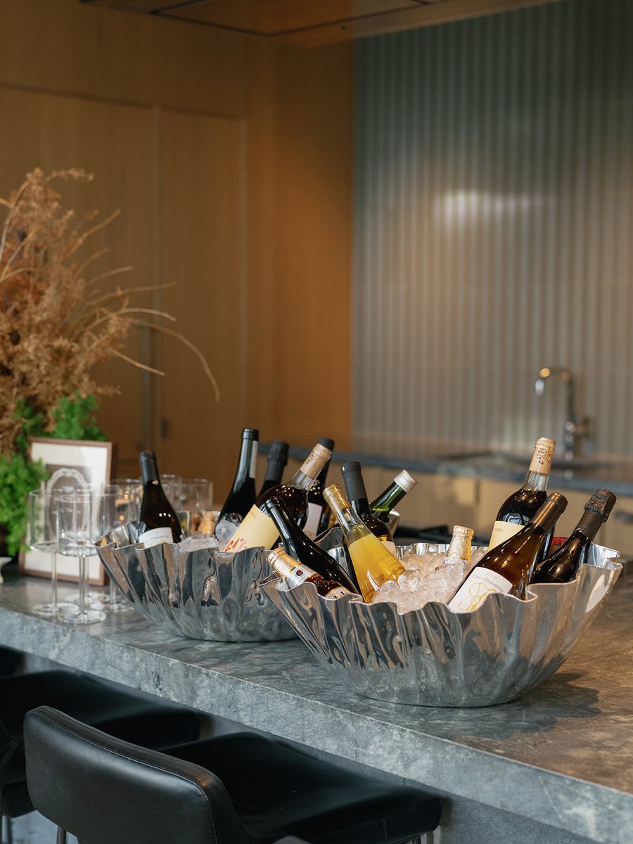 Two large, fluted silver ice buckets filled with various wine and champagne bottles are displayed on a sleek stone bar c