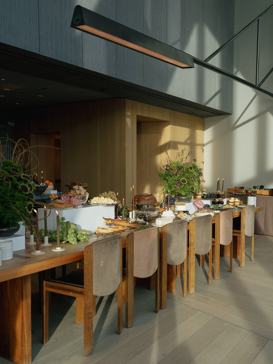 A long, beautifully arranged buffet table is laden with an assortment of food, including cheeses, charcuterie, and desse