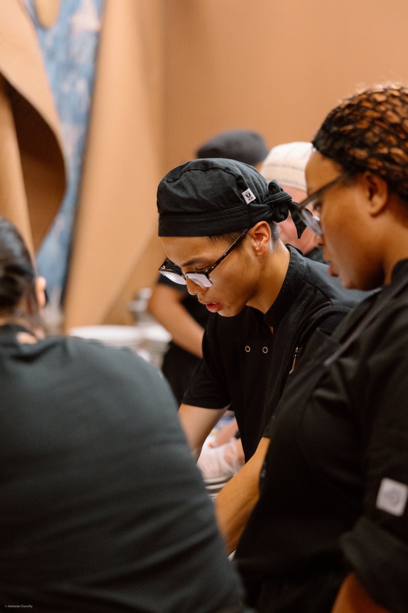 A close-up, candid shot captures several kitchen staff members, likely chefs, intently focused on preparing food at a st