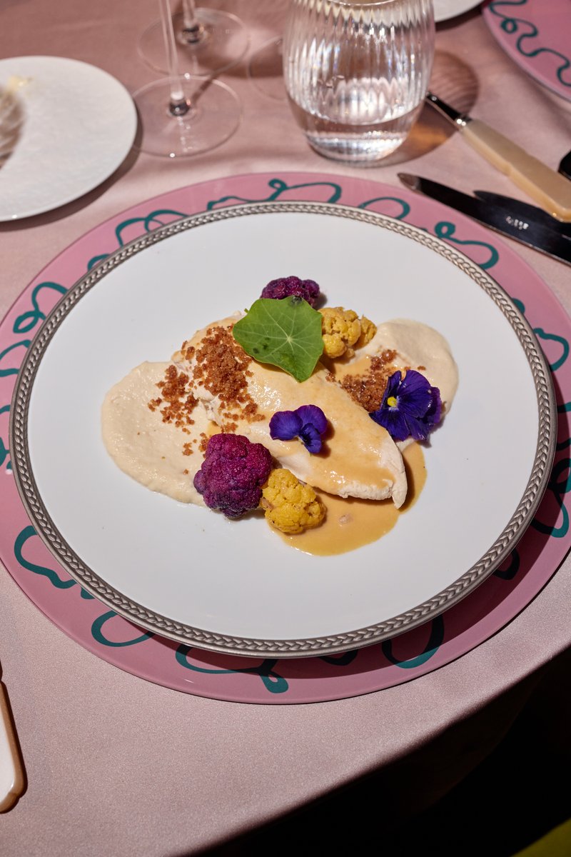 A beautifully plated dish featuring what appears to be chicken or fish with a creamy sauce, garnished with vibrant purpl