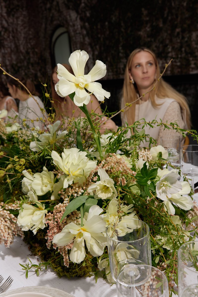 A vibrant floral centerpiece, featuring an array of white and cream flowers with lush green foliage, dominates the foreg