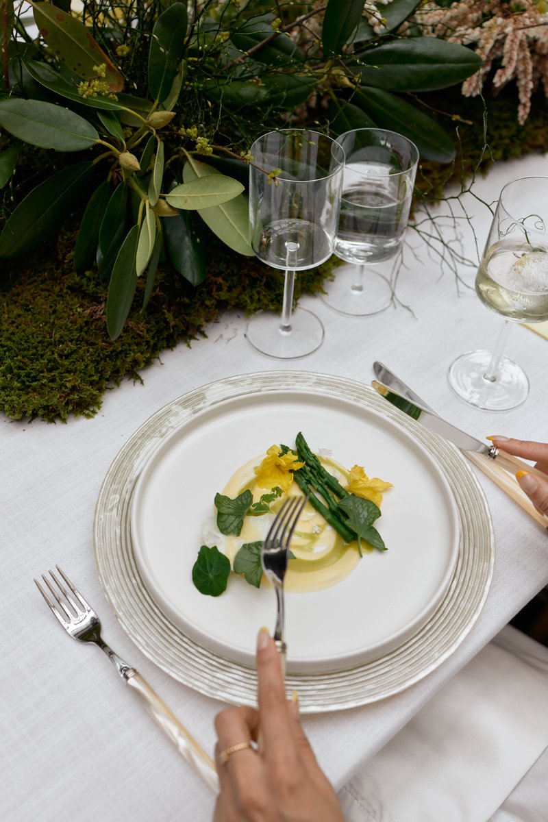A close-up shot captures a beautifully plated dish featuring asparagus, yellow edible flowers, and a creamy sauce, set o
