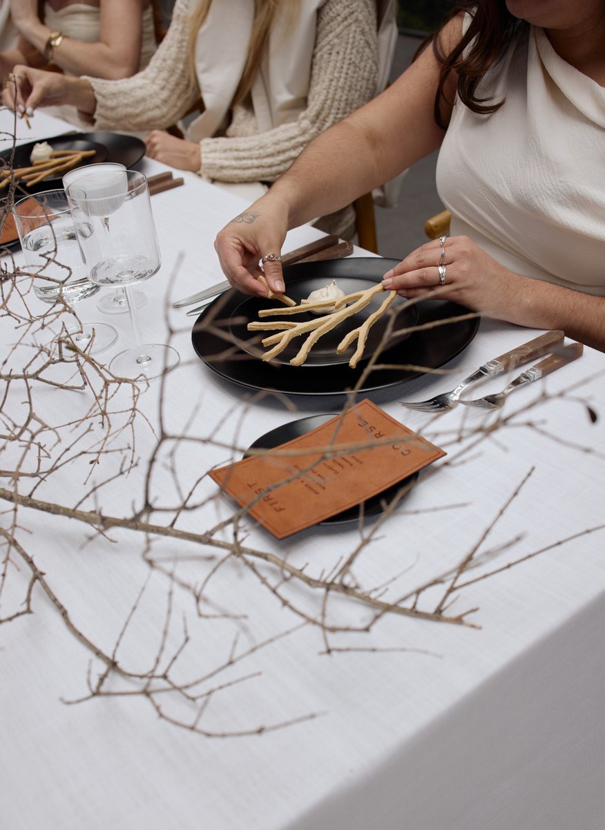 A close-up shot captures a guest meticulously arranging branch-shaped crackers and a white dip on a black plate at an el