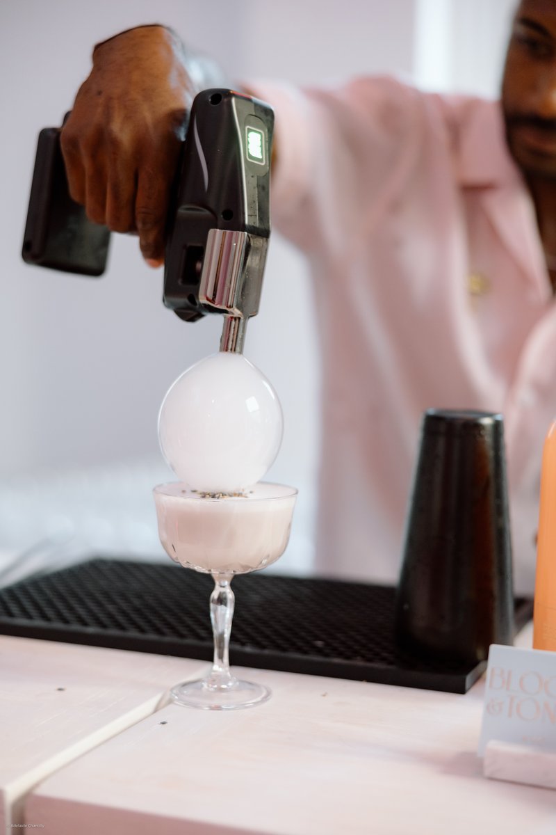 A bartender is expertly crafting a unique cocktail, using a specialized device to create a large, ethereal smoke bubble 