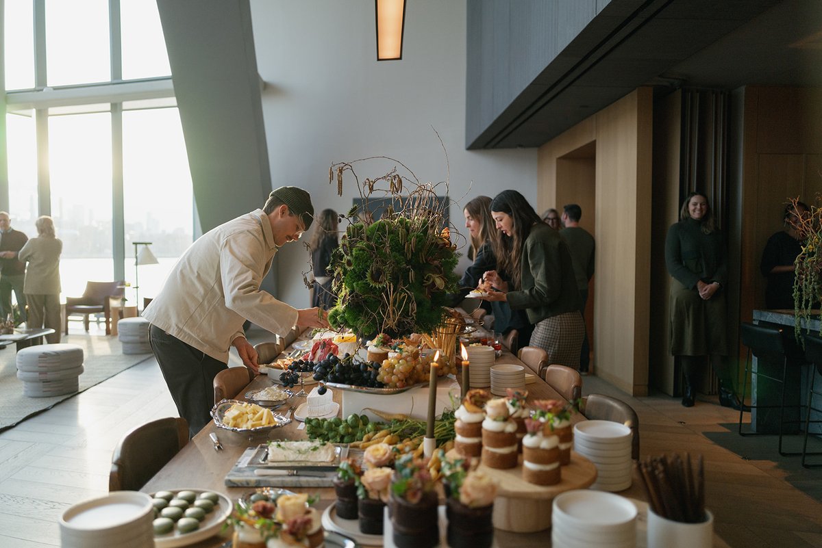 Guests are seen serving themselves from an elaborate buffet table laden with various food items and desserts. The settin