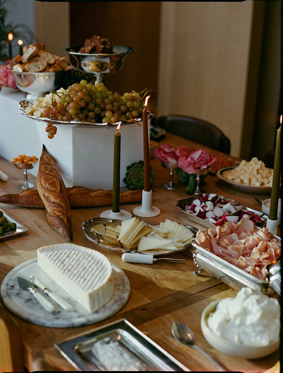 A beautifully arranged dinner table is laden with a gourmet spread, featuring various cheeses, cured meats, grapes, and 