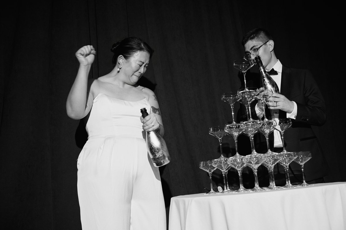 A black and white photo captures a celebratory moment as a man in a tuxedo pours champagne into a towering pyramid of co