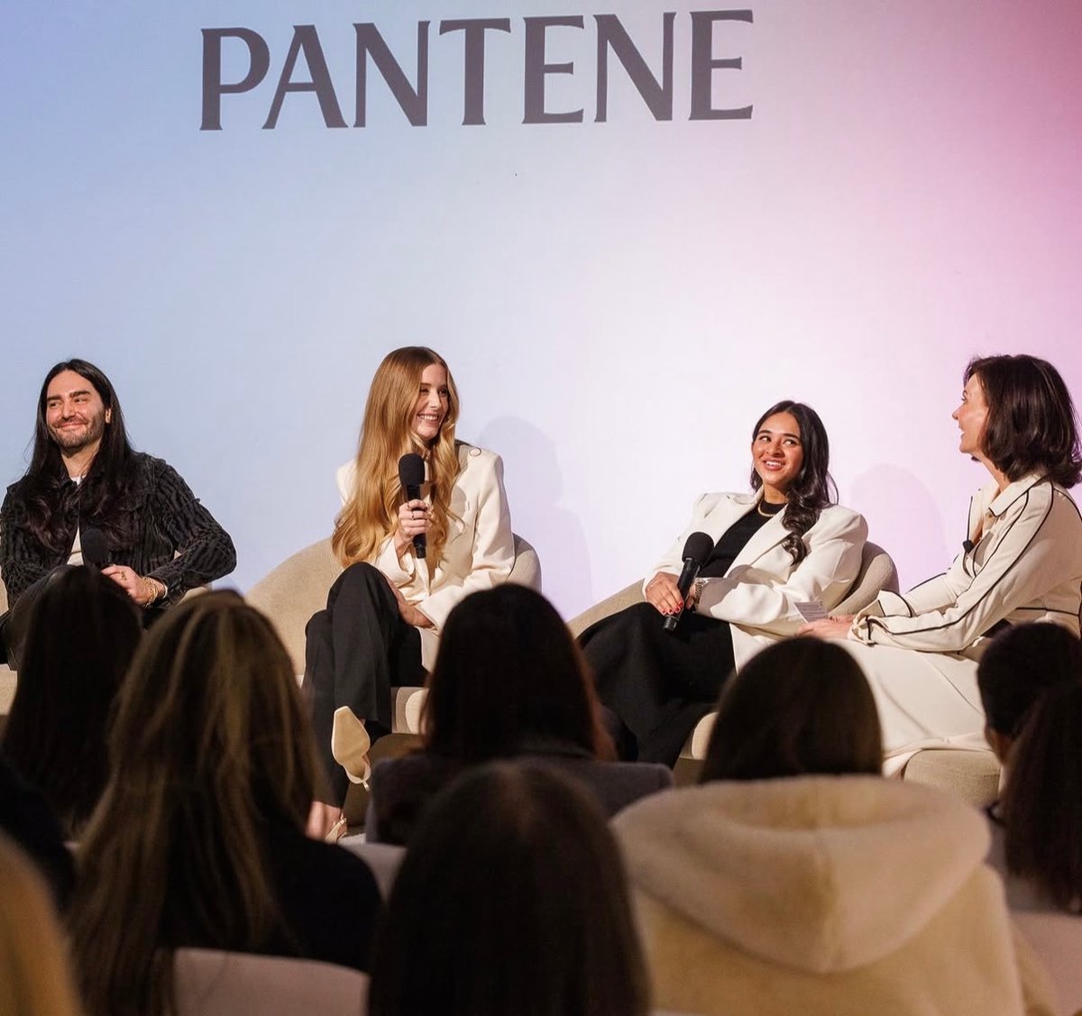 Four panelists, three women and one man, are seated on a stage, actively participating in a discussion. They are holding