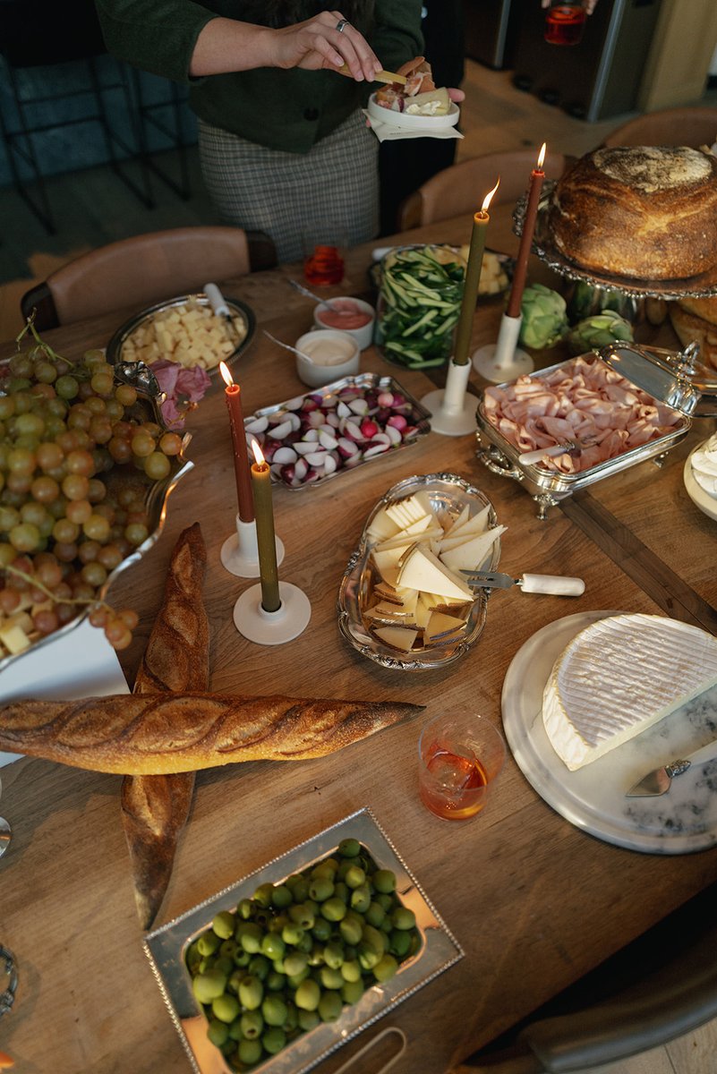 A person serves themselves from a bountiful appetizer spread laid out on a wooden table. The table is laden with various