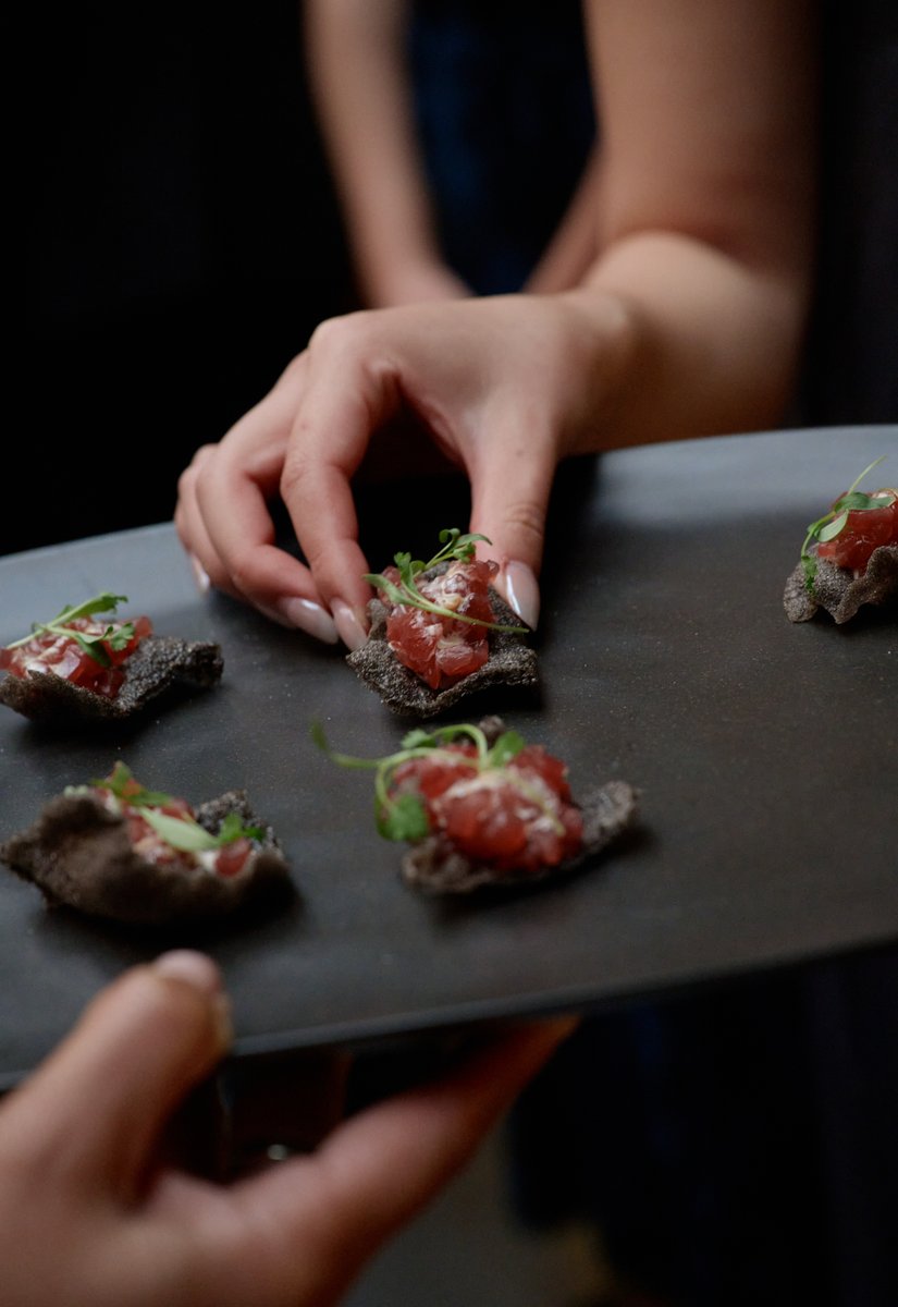 A close-up shot captures a server's hand delicately arranging or presenting small appetizers on a dark rectangular tray.