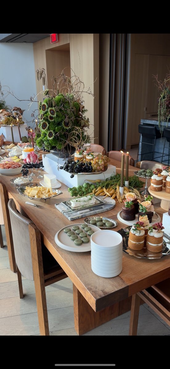 An elegantly arranged buffet table showcases a variety of appetizers and desserts. The long wooden table is laden with c