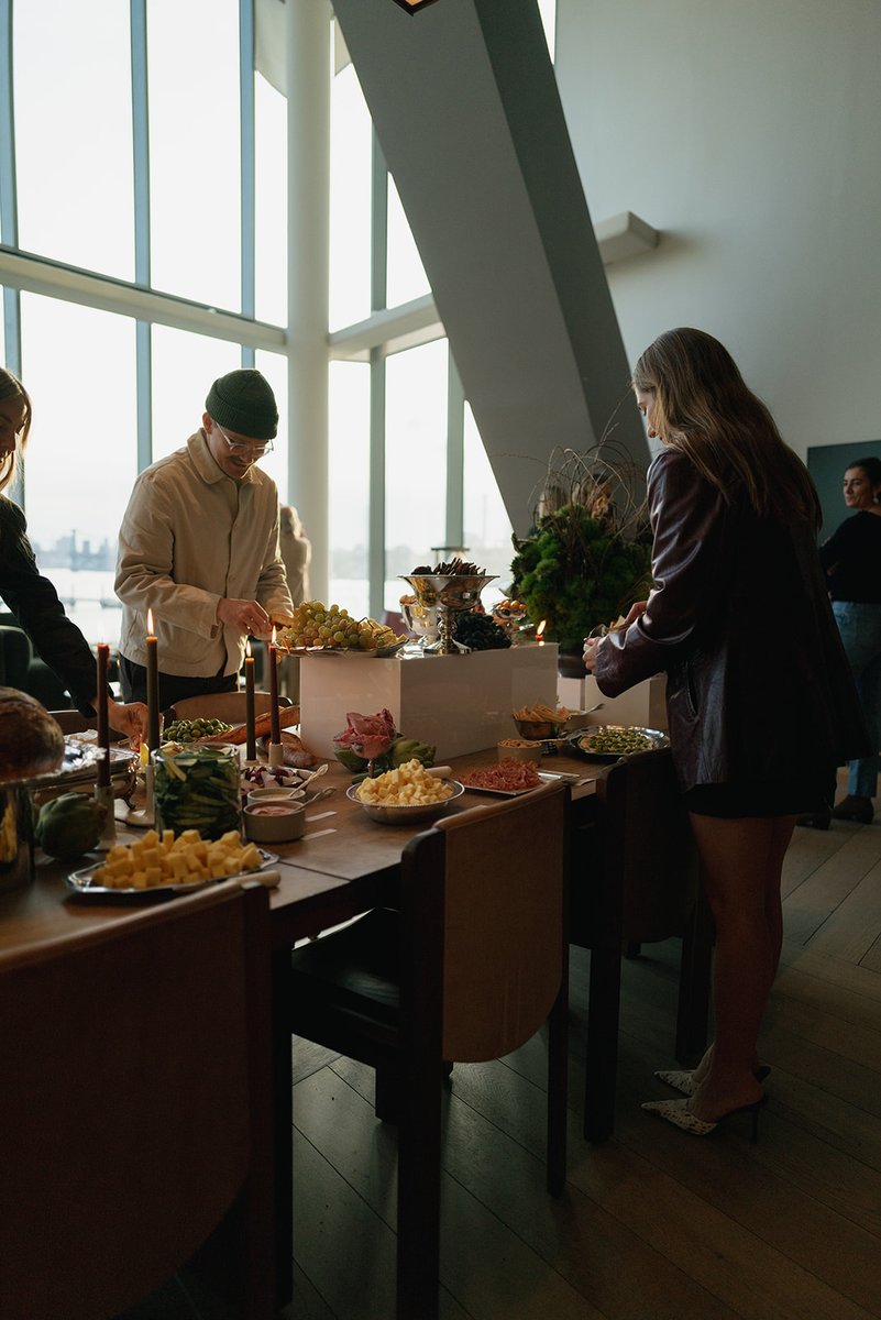 Guests gather around a long buffet table, serving themselves from an array of appetizers and snacks. The scene is set in