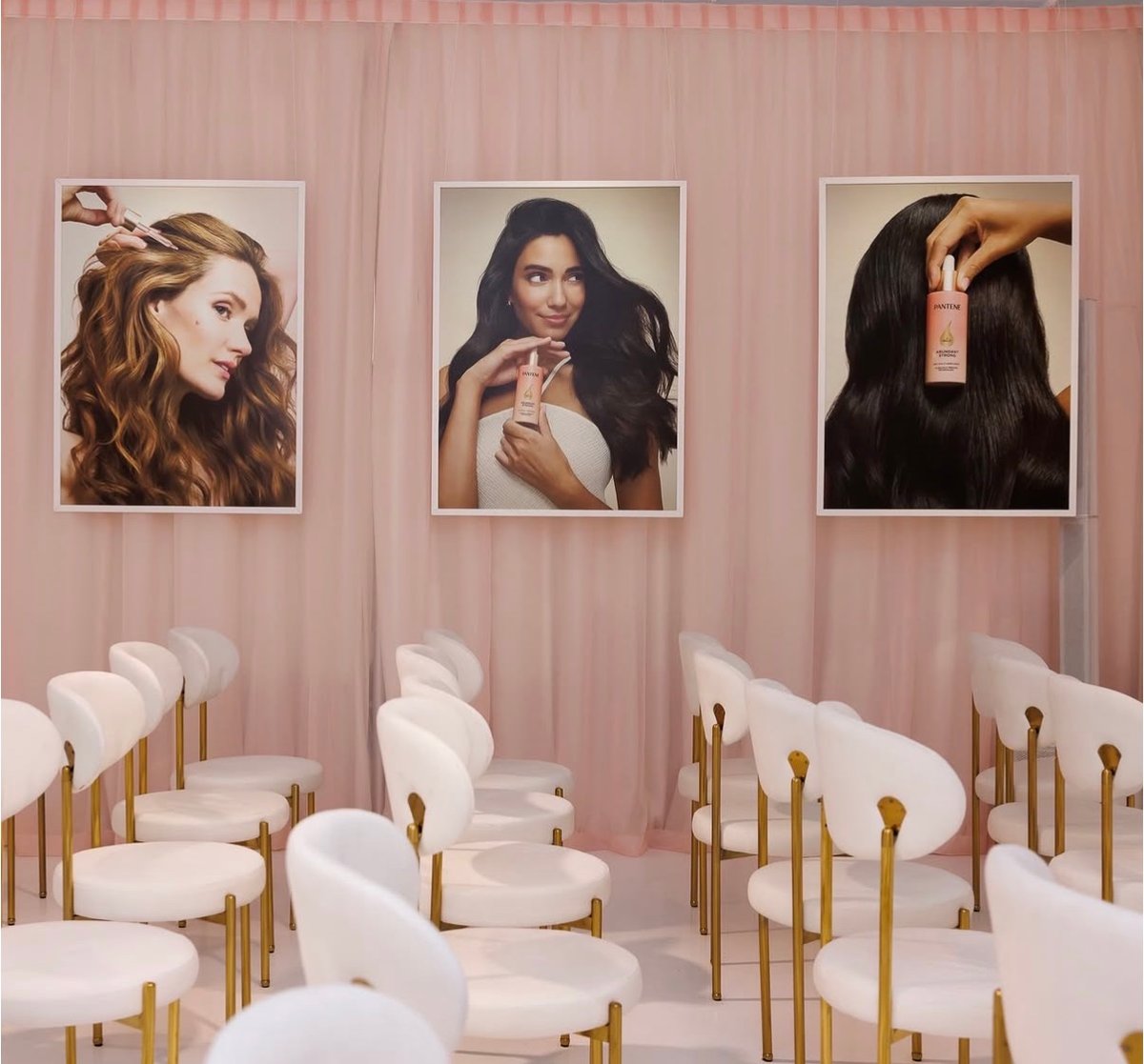 This photo captures an event space adorned with blush pink curtains and rows of elegant white and gold chairs, set up fo