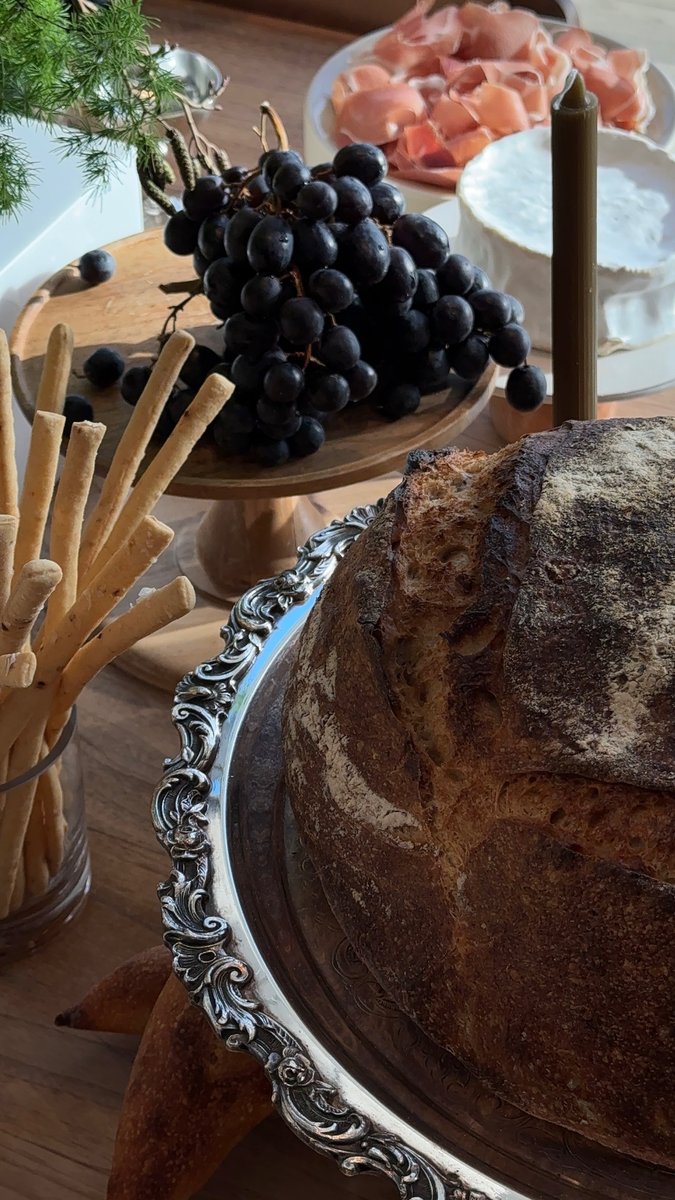 A close-up shot captures an inviting gourmet spread featuring a large loaf of artisan bread on an ornate silver platter.