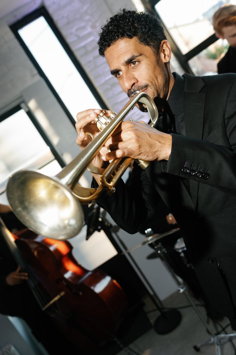 A focused musician, dressed in a black suit, plays a brass trumpet with intensity. The dynamic shot captures him mid-per