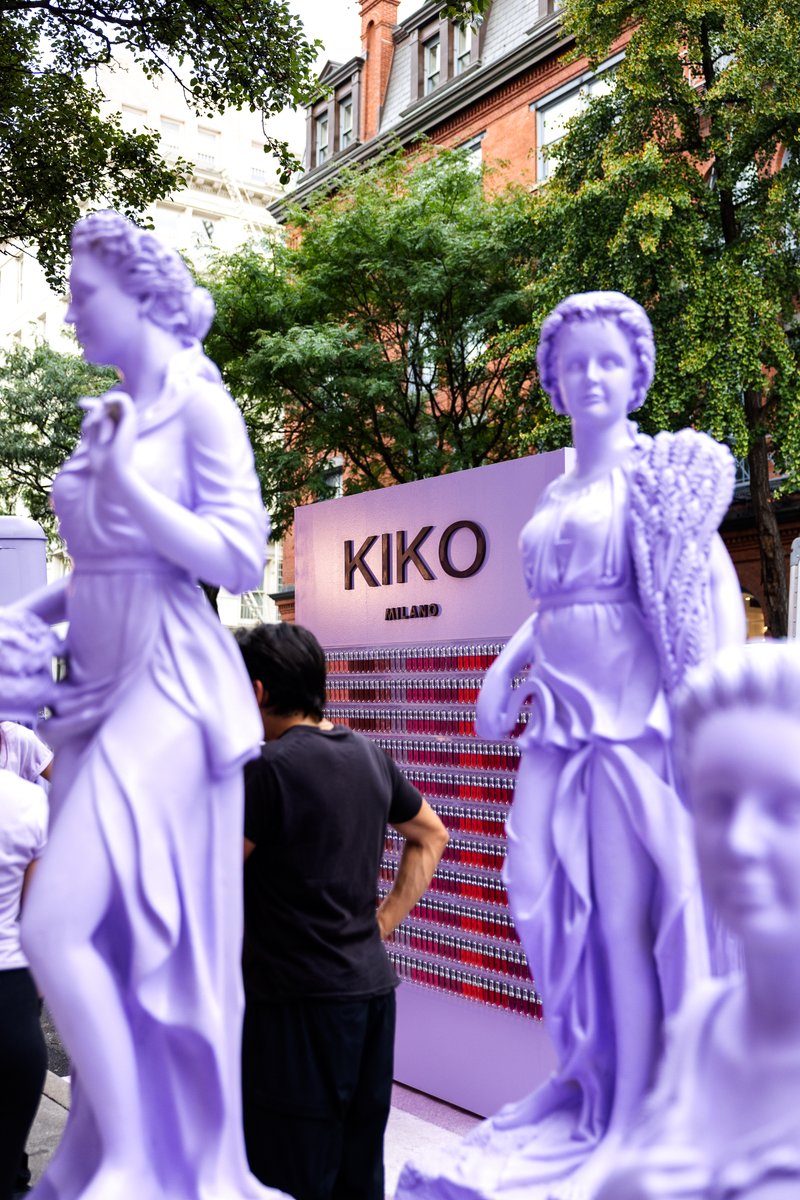This photo showcases an outdoor event setup, featuring several large, purple classical statues in the foreground and mid