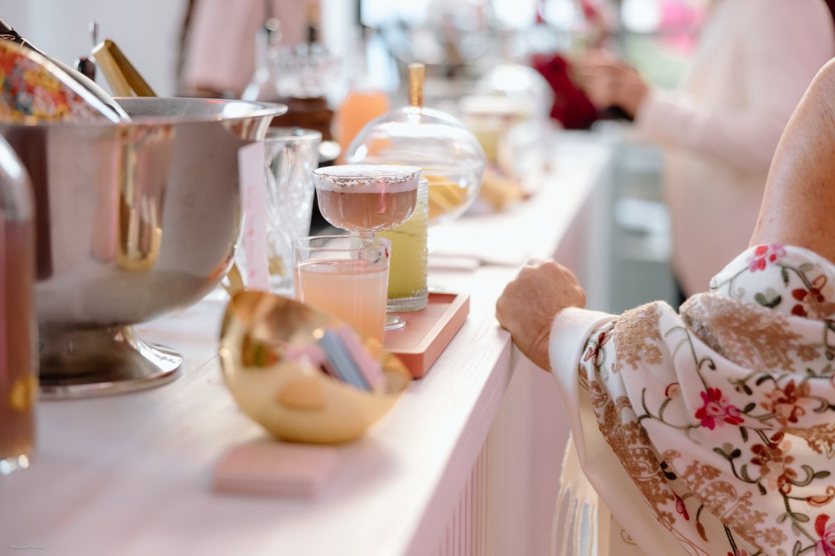 A close-up, candid shot captures a vibrant drink station at an event, showcasing various colorful cocktails and a silver