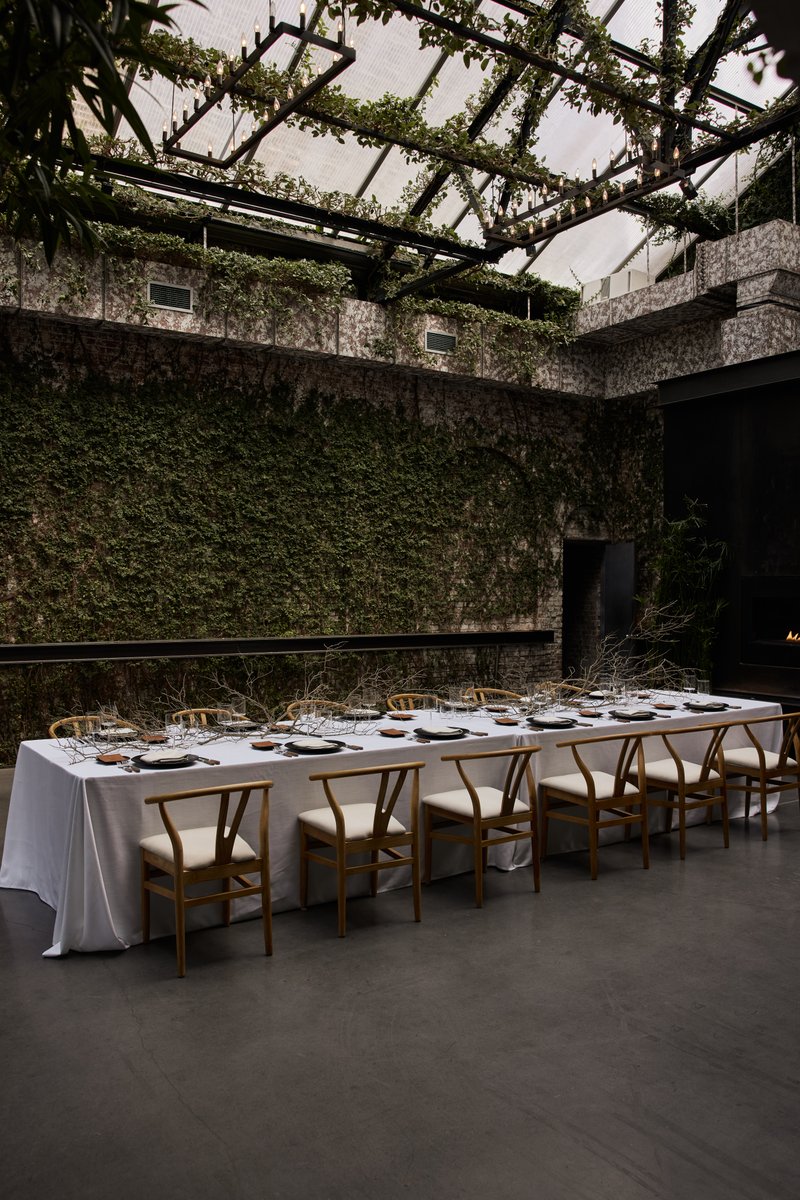 A long dining table, elegantly set with modern place settings and natural branch decor, is positioned in a unique venue.