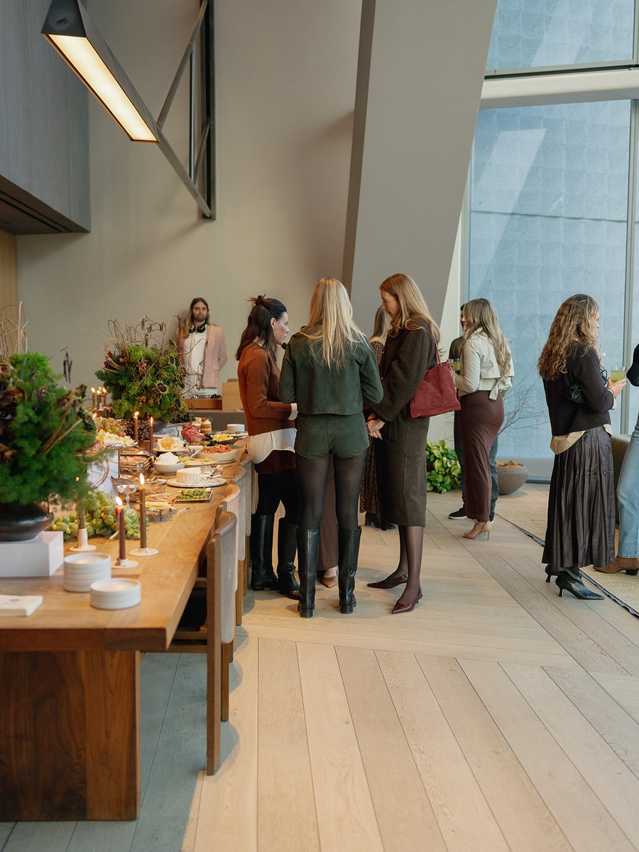 Guests are gathered around a beautifully arranged food station at a modern event space. Several women are seen conversin