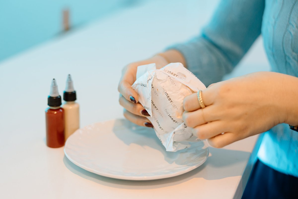 A close-up shot shows a person's hands unwrapping a white, branded package, possibly containing a snack or food item. An