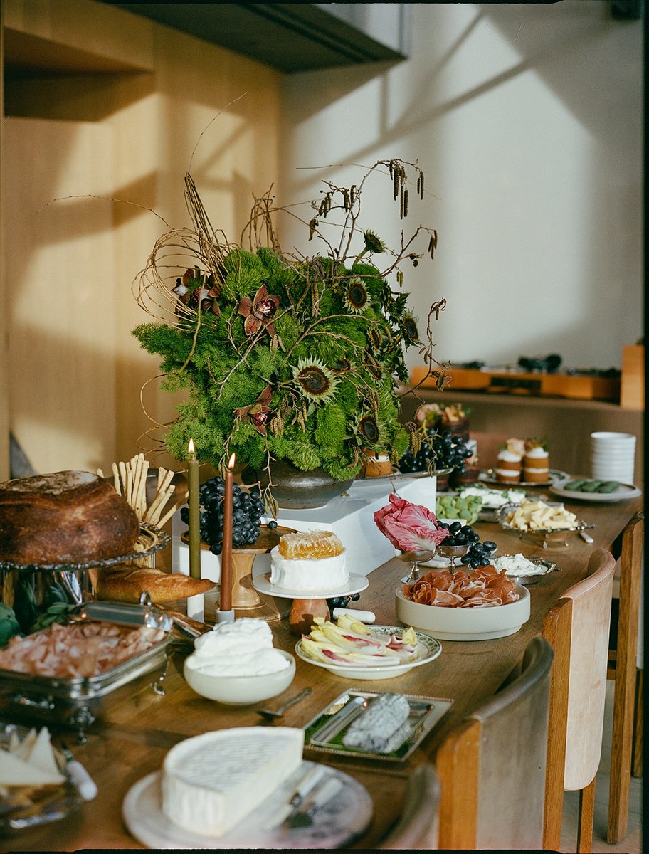 A beautifully arranged buffet table is laden with an assortment of gourmet foods, including cheeses, cured meats, bread,