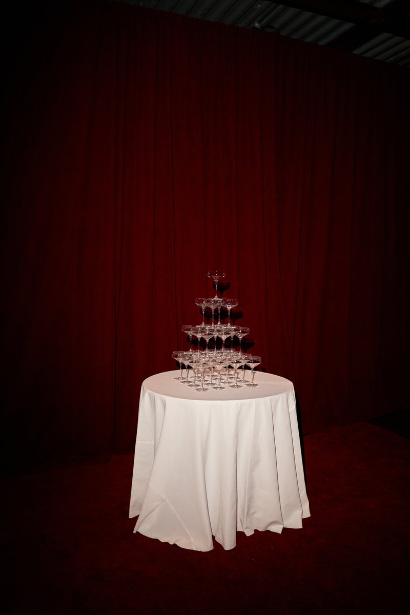 A classic champagne coupe tower is meticulously set up on a round table draped with a crisp white tablecloth. The elegan