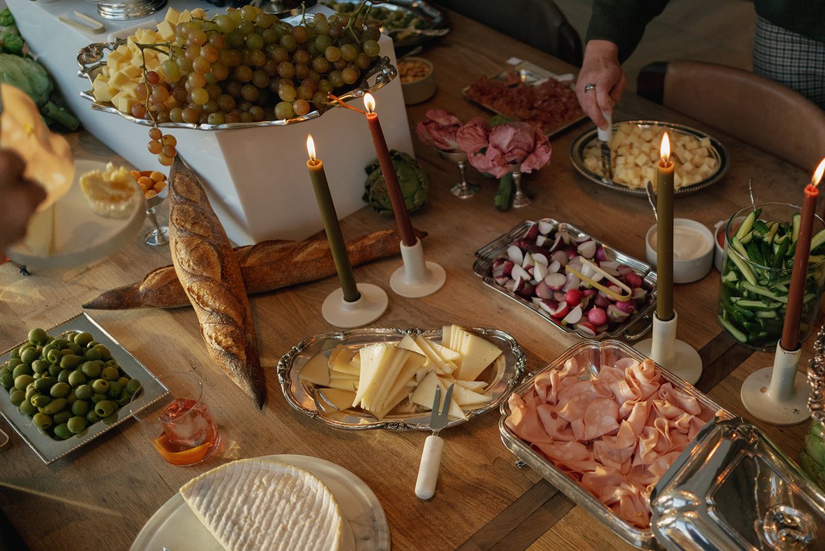 A beautifully arranged gourmet appetizer table features an array of cheeses, cured meats, fresh grapes, olives, and bagu