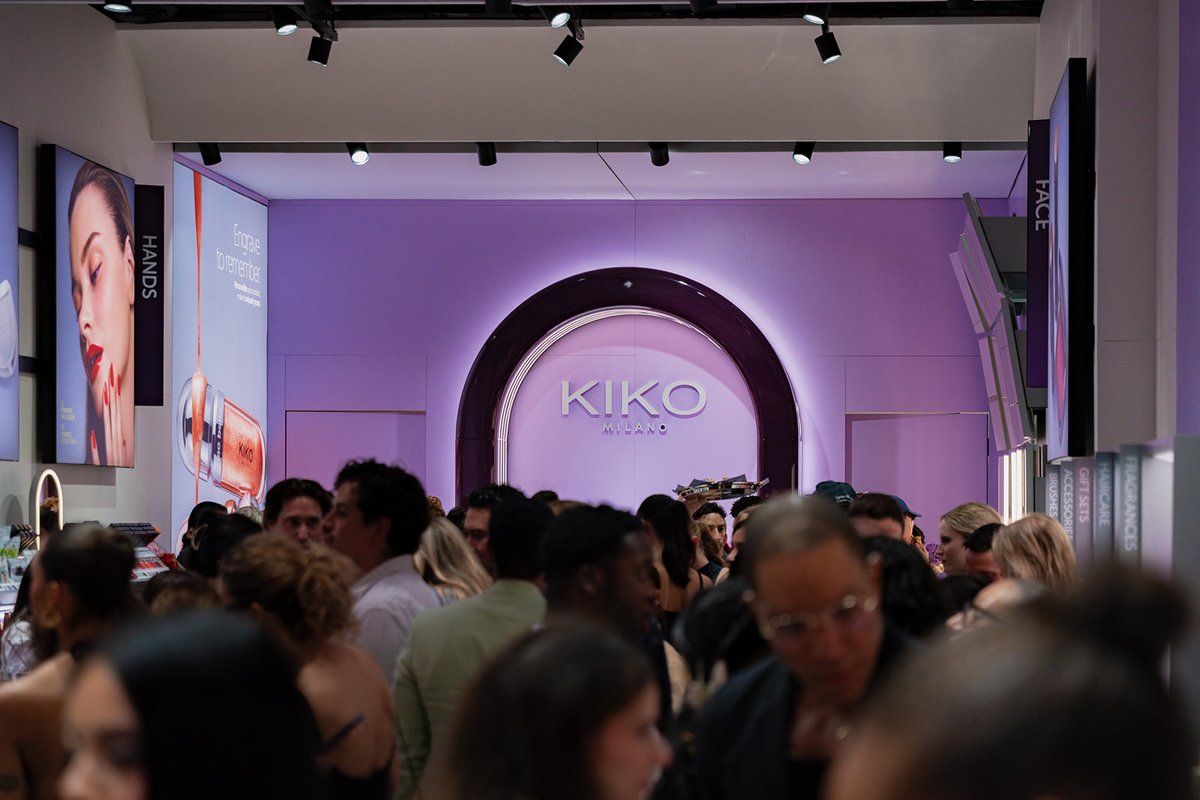 A bustling crowd gathers inside a Kiko Milano store, with the brand's logo prominently displayed on a purple-lit arched 