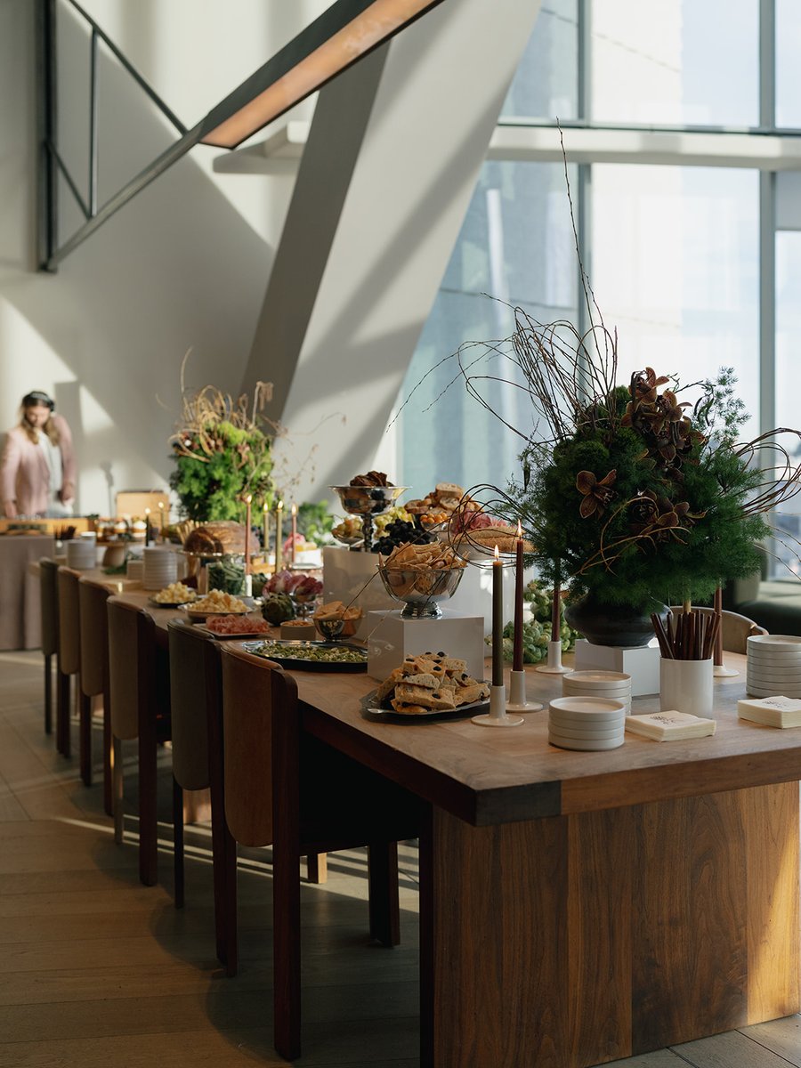 A beautifully arranged buffet table is set up in a modern, sunlit venue, featuring a variety of appetizers and snacks. T
