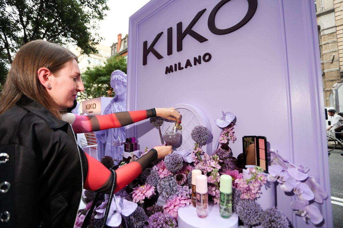 A guest in a black jacket and red-striped sleeves pours a purple drink from a dispenser at a KIKO Milano brand activatio
