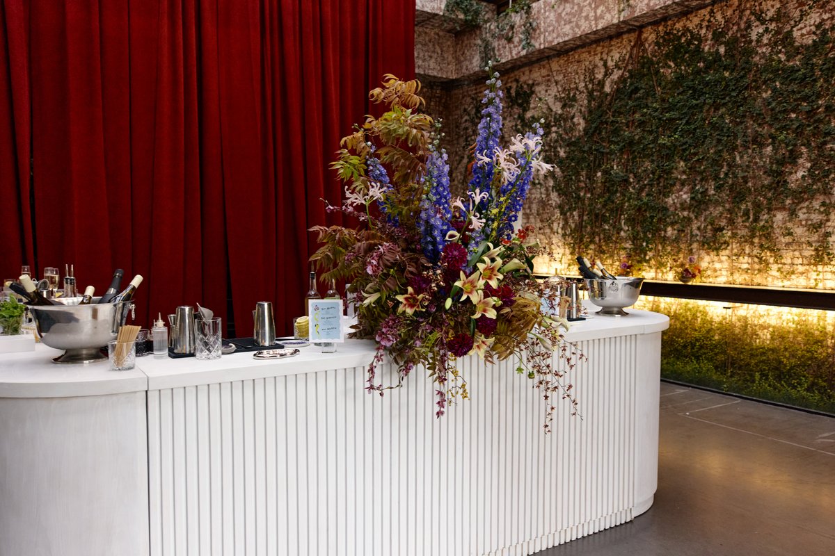 This photo captures a stylish bar setup featuring a white fluted bar counter adorned with a large, vibrant floral arrang