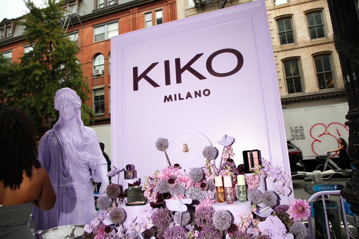 An outdoor product display for Kiko Milano features a large purple sign, a matching purple statue, and an elaborate flor