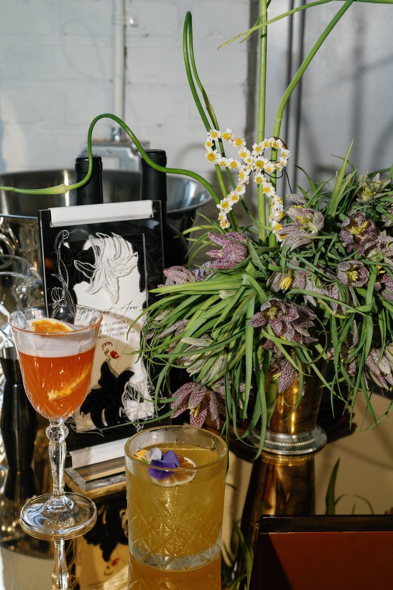Two vibrant cocktails, one orange with a frothy top and citrus garnish, and another yellow with an edible flower and lim