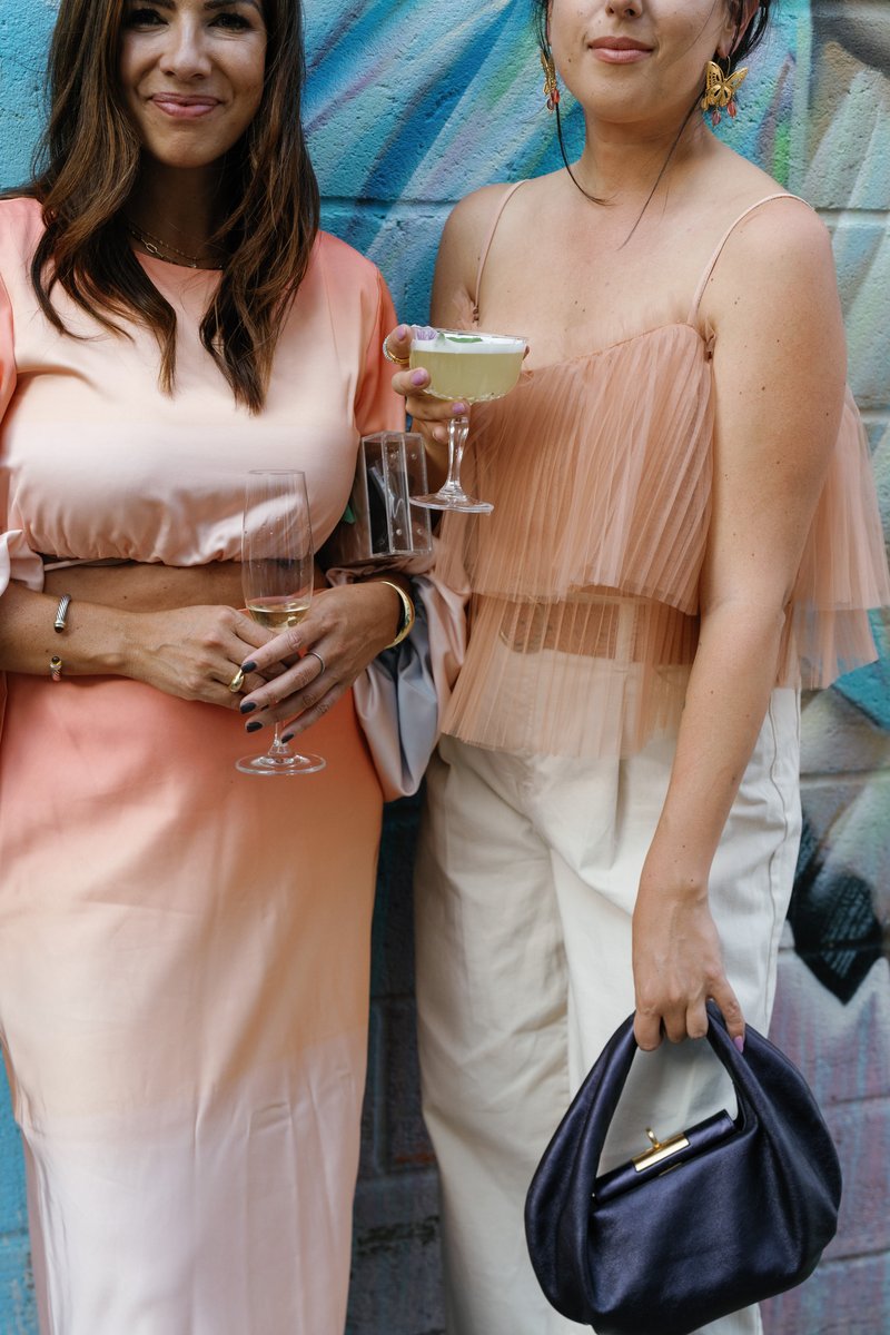 Two women, likely guests, are captured in a medium shot, holding drinks and smiling against a vibrant, graffiti-style pa
