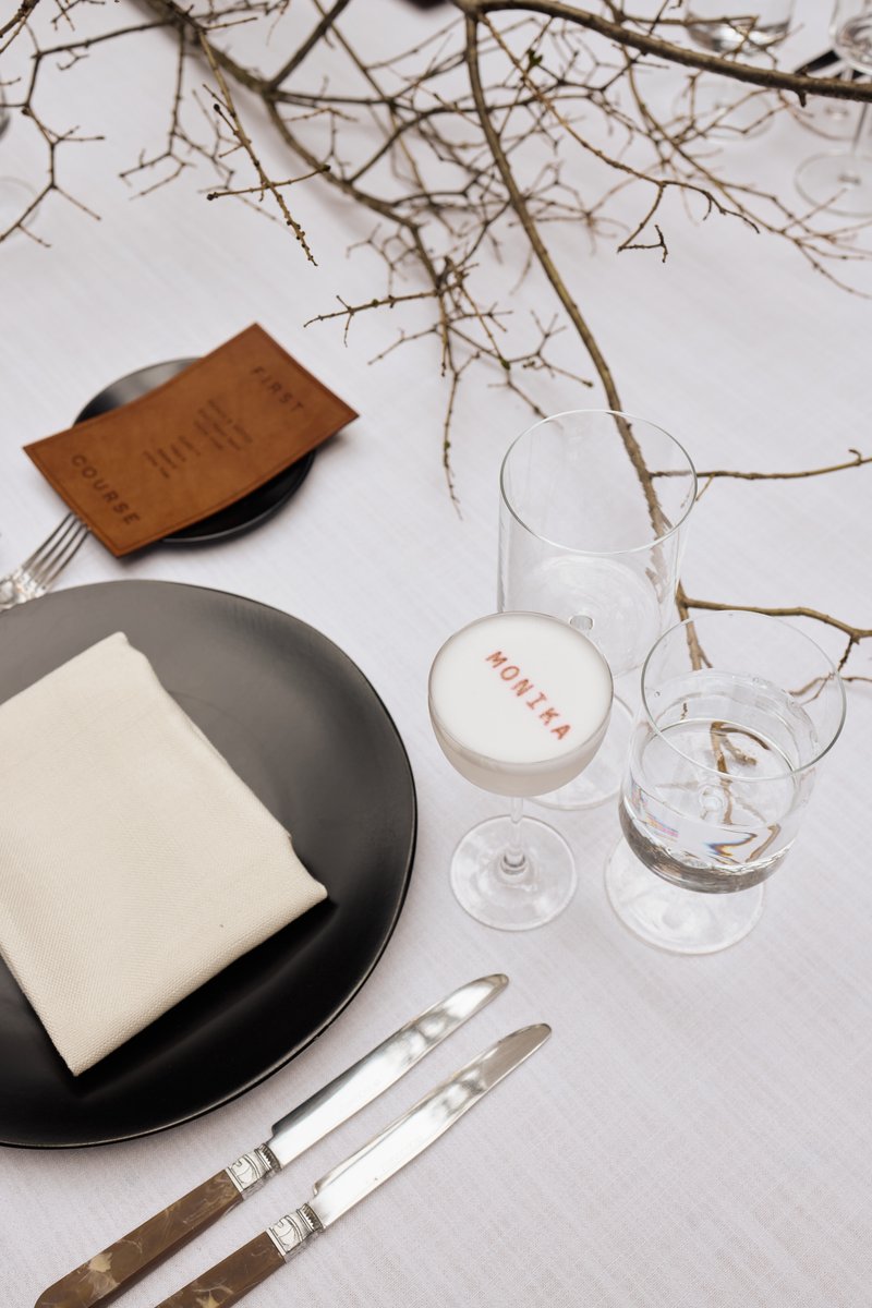 A sophisticated table setting is captured from an overhead perspective, featuring a personalized white cocktail with 'MO