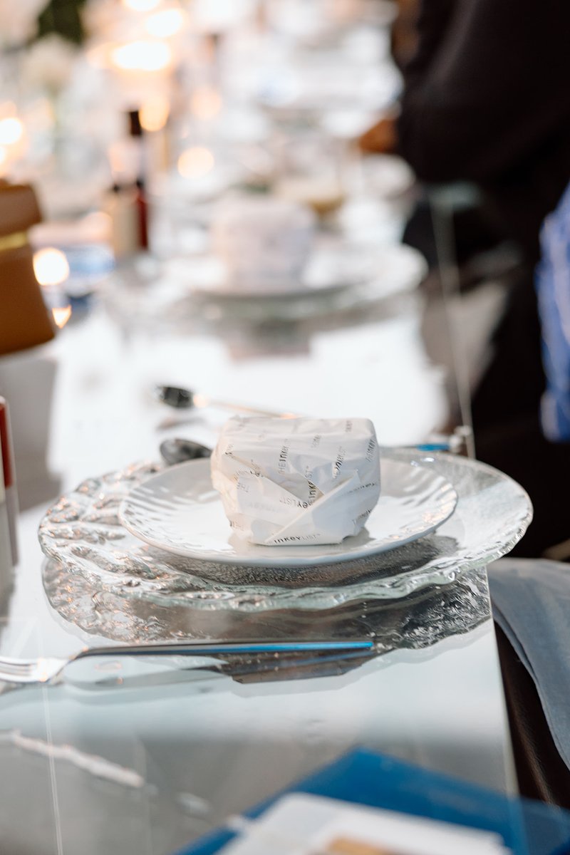 A close-up shot showcases an elegant table setting with a clear glass charger plate and a white dinner plate. A small wr