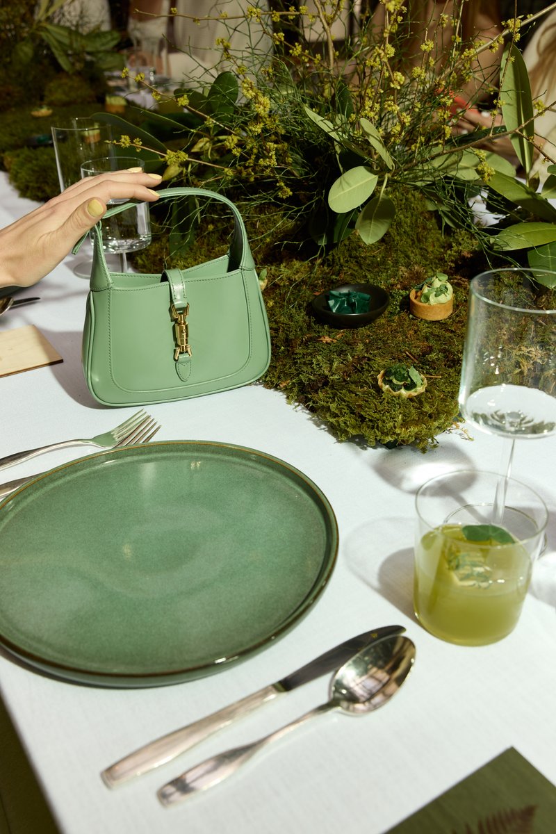A guest's hand with yellow nail polish reaches for a light green handbag placed on a beautifully decorated table. The ta