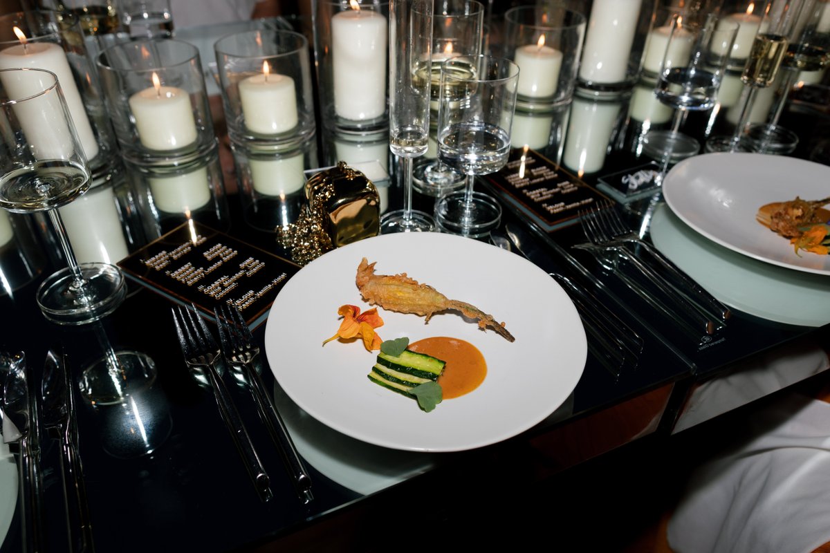 An elegant table setting features individual plates with artfully presented food, surrounded by numerous flickering cand