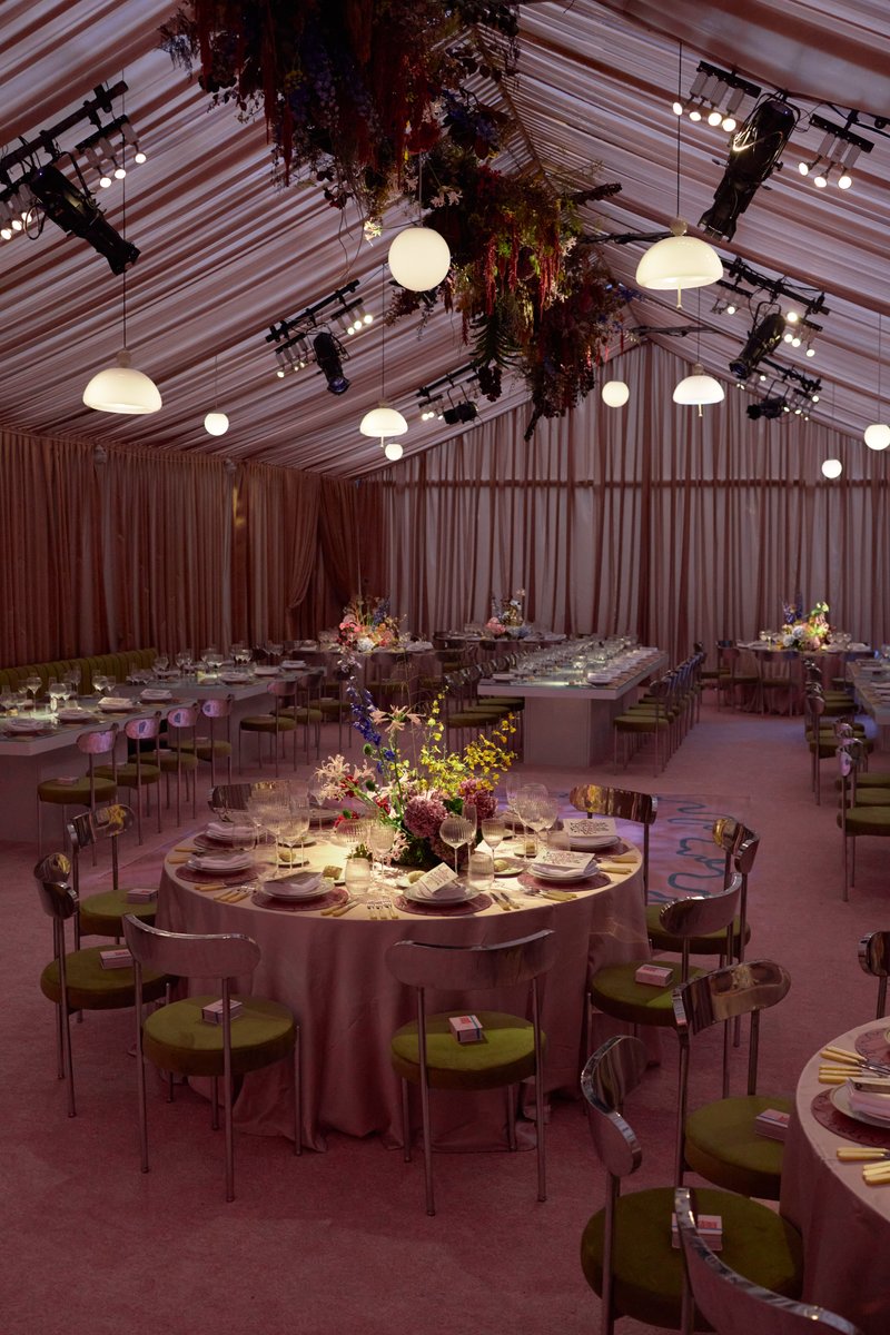 This wide shot captures an elegantly set event space within a tent, featuring multiple round and rectangular tables ador