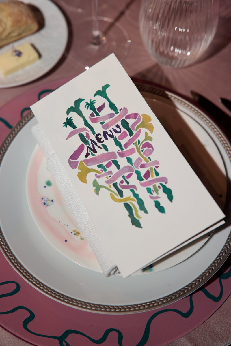 A close-up shot captures a beautifully arranged place setting, featuring a custom menu card with vibrant, artistic lette