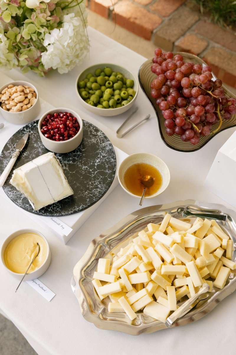 An inviting spread of gourmet cheeses, fresh fruits, and accompaniments is beautifully arranged on a white tablecloth. T