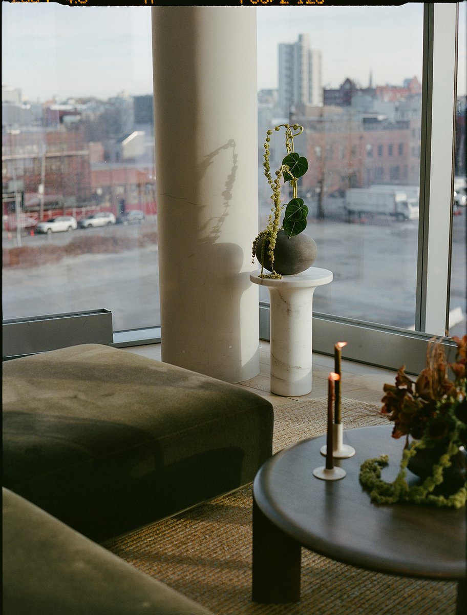 A modern lounge area is captured, featuring a dark green velvet ottoman and a round coffee table with lit candles and a 