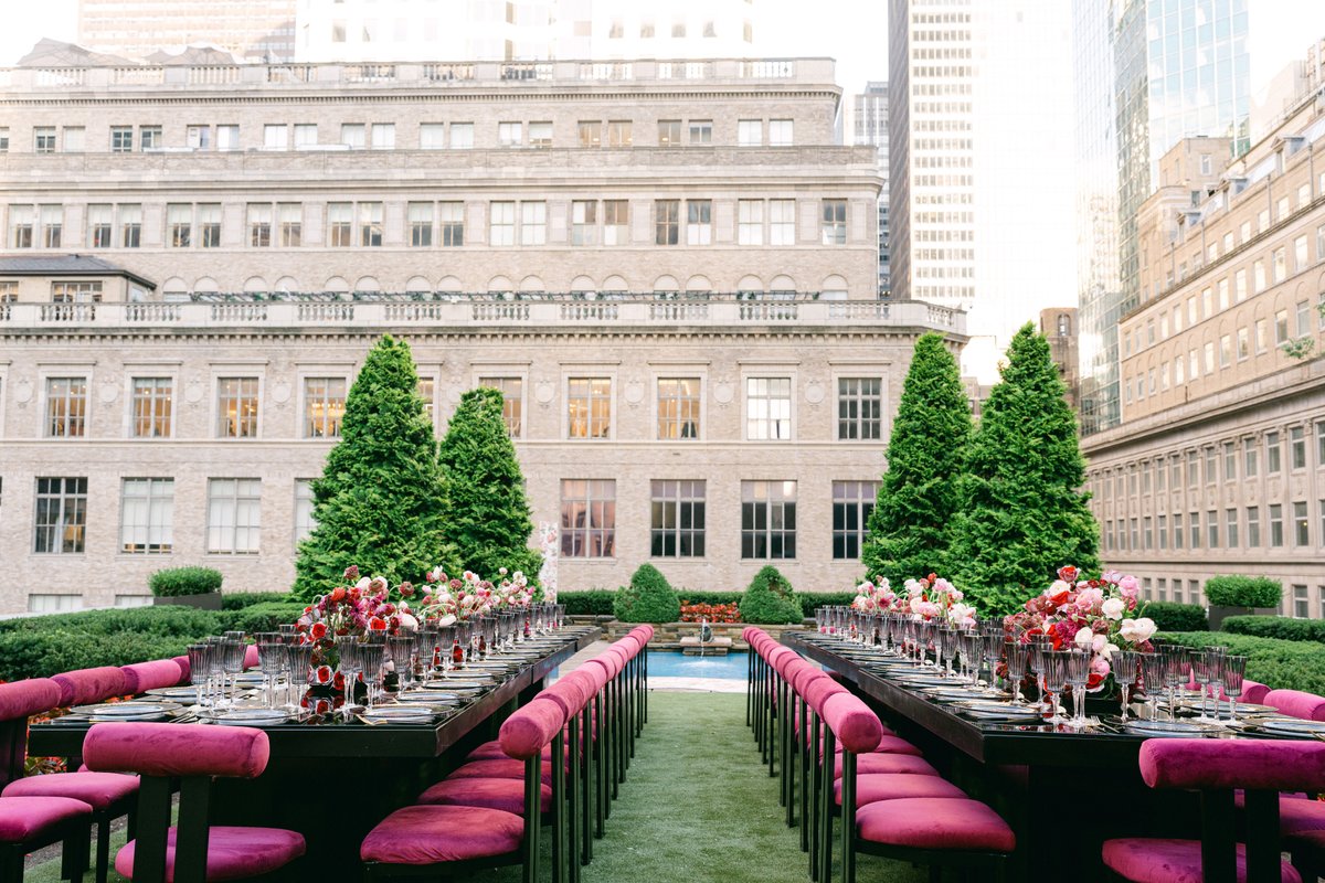 This photo captures an elegant outdoor event setup on a rooftop, featuring two long dining tables meticulously arranged 