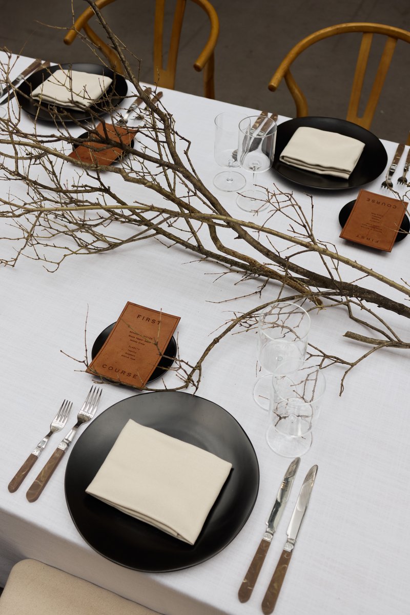 An overhead medium-shot captures a elegantly set table for an event, featuring minimalist decor with bare branches stret