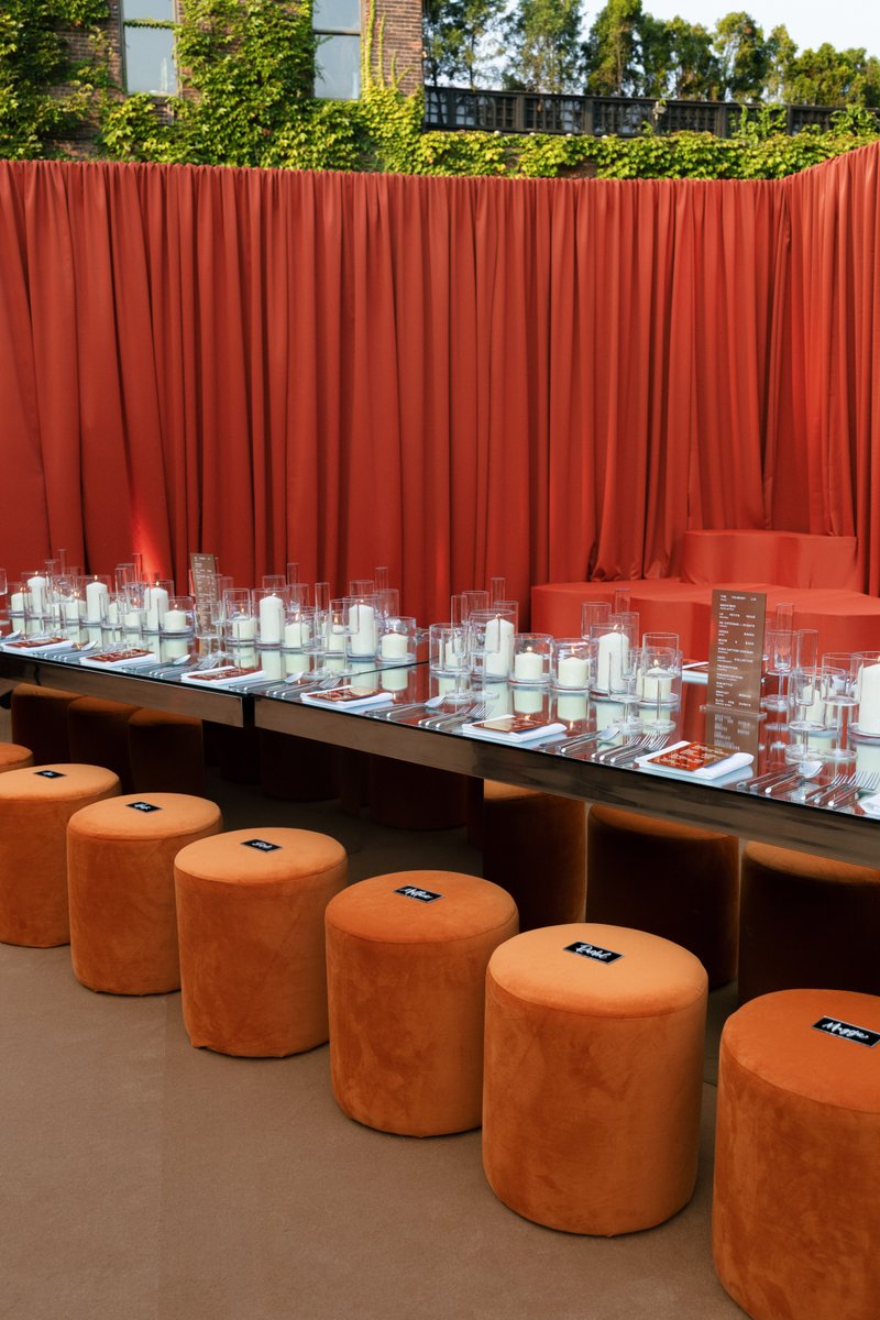 A long, modern dining table with a mirrored surface is meticulously set with candles, glassware, and cutlery, ready for 