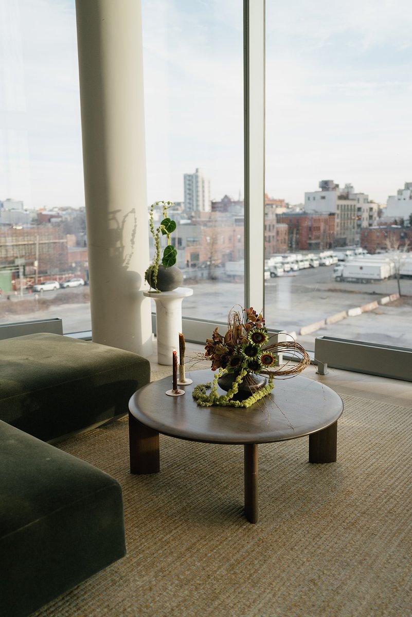 A modern lounge area features a round coffee table with an elaborate floral arrangement and candles, alongside a plush g